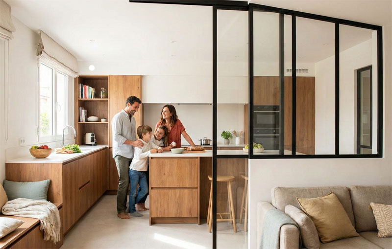 Une famille réunie dans une cuisine moderne boisée, séparée du salon par une élégante verrière en acier noir avec porte coulissante.