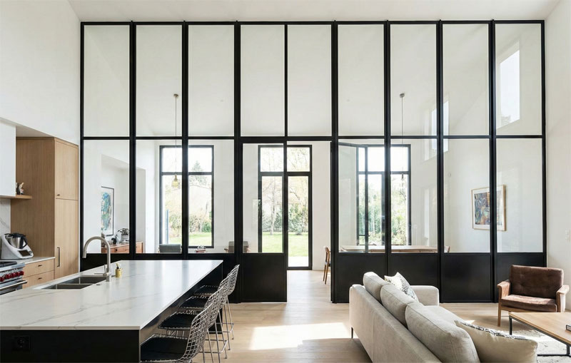 Grande verrière toute hauteur en métal noir avec porte battante centrale pour un intérieur à haut plafond.