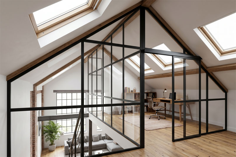 Une vue architecturale en contre-plongée depuis un escalier en bois, regardant vers une mezzanine lumineuse sous les combles. Une grande verrière d'atelier à montants noirs divise l'espace, abritant un bureau d'ordinateur, une bibliothèque et une chaise. Le niveau inférieur est visible à travers les vitrages du sol, créant un espace de vie ouvert et transparent avec poutres apparentes et multiples fenêtres de toit.